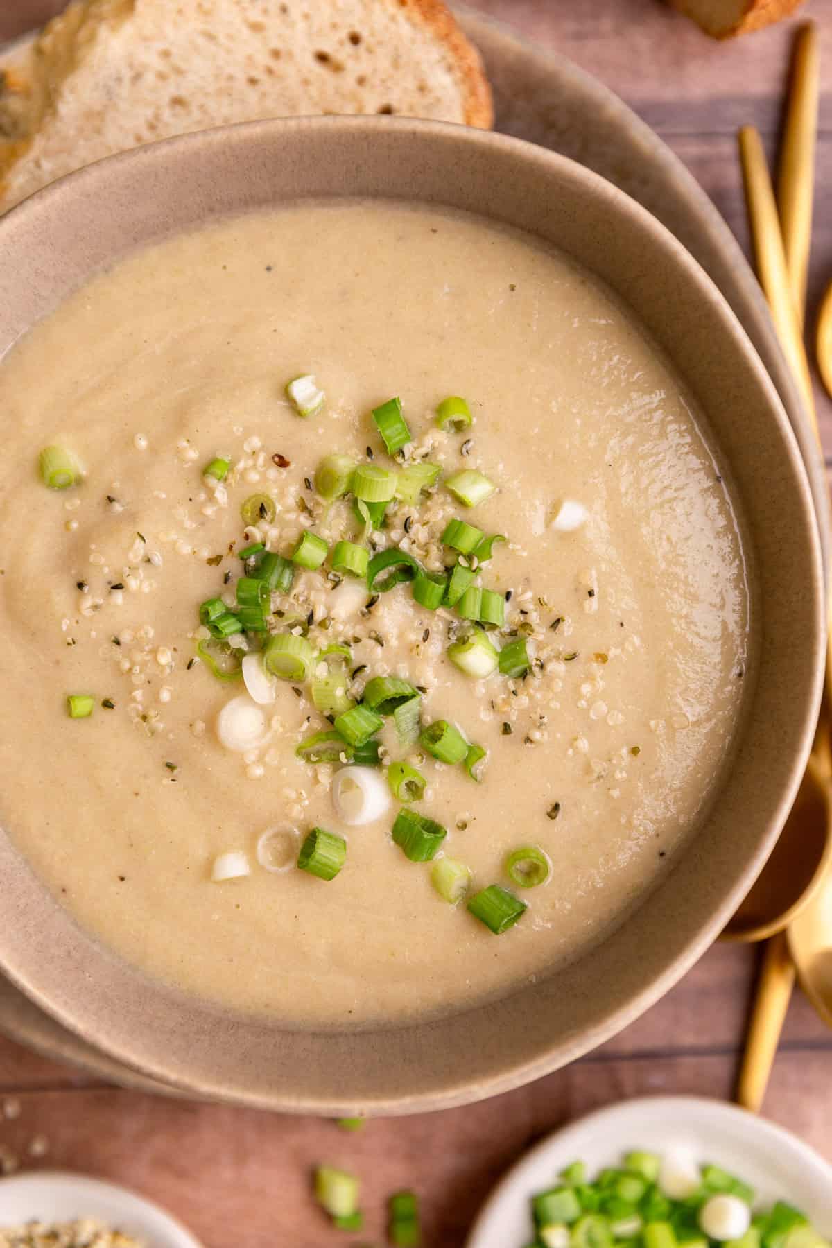 A bowl of vegan celery soup, garnished with scallions and hemp seeds.