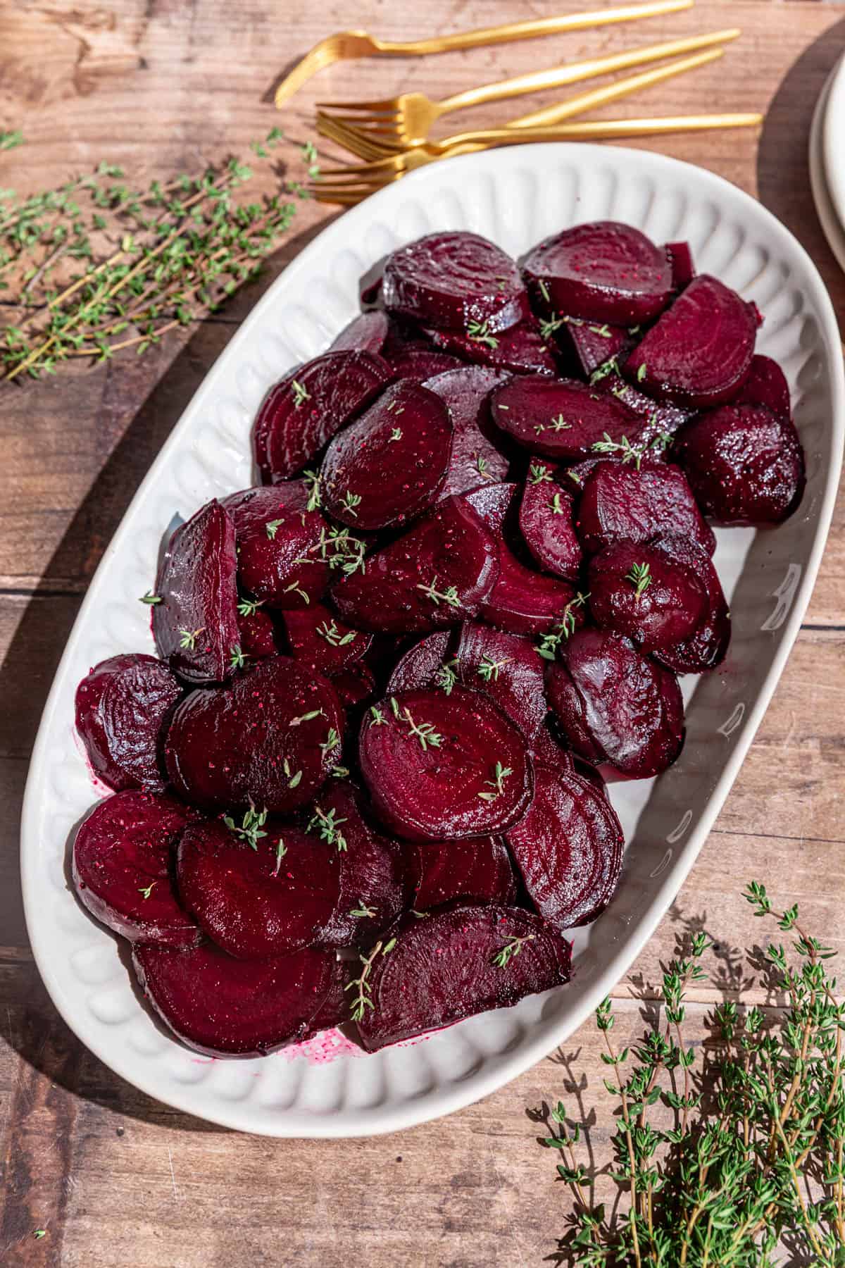 A platter of roasted beets, garnished with fresh thyme leaves, with a few plates and forks, ready to serve.