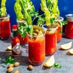 Several bloody mary glasses, with lemon wedges, olives, and celery.