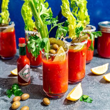 Several bloody mary glasses, with lemon wedges, olives, and celery.