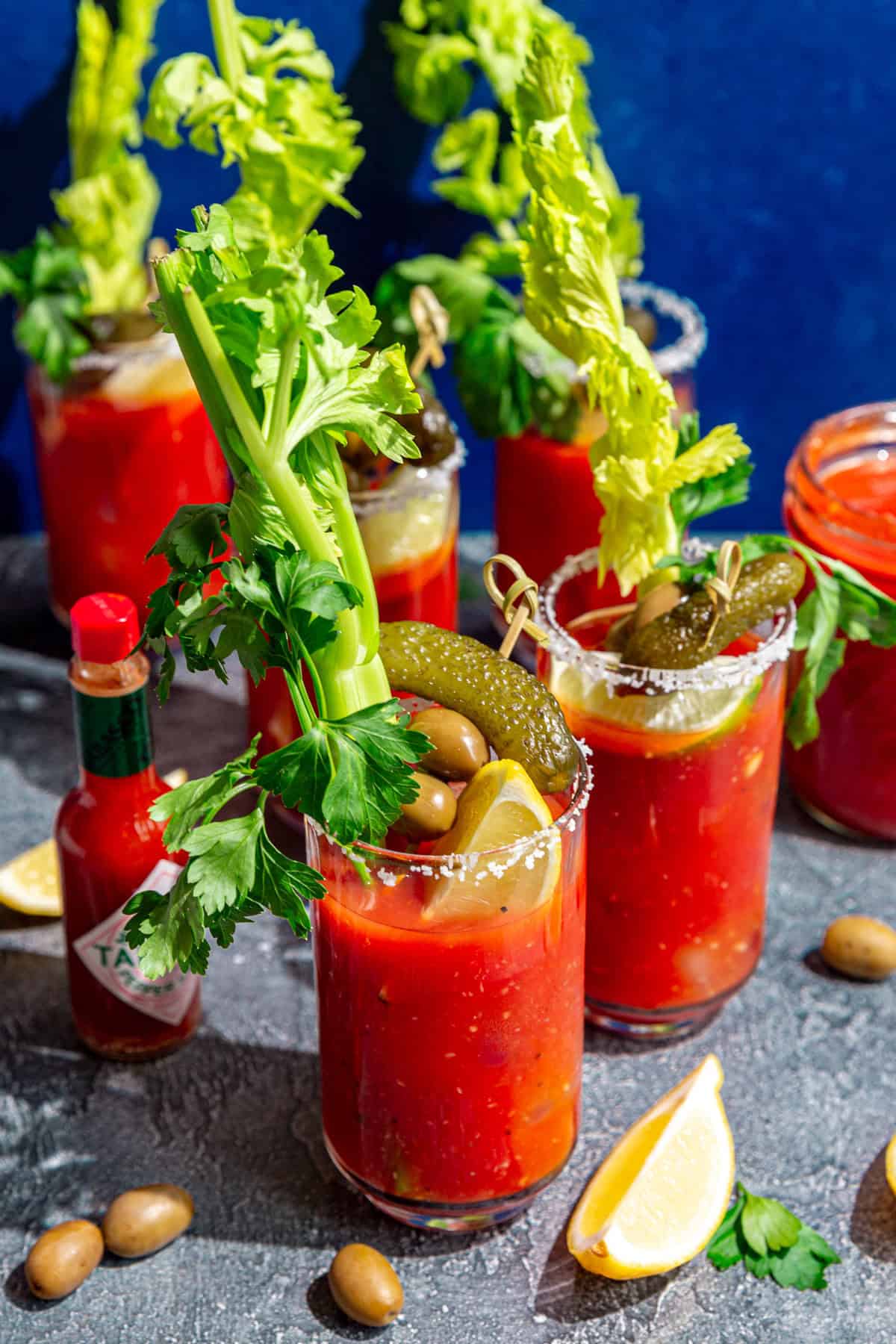 Several bloody mary glasses, with lemon wedges, olives, and celery.