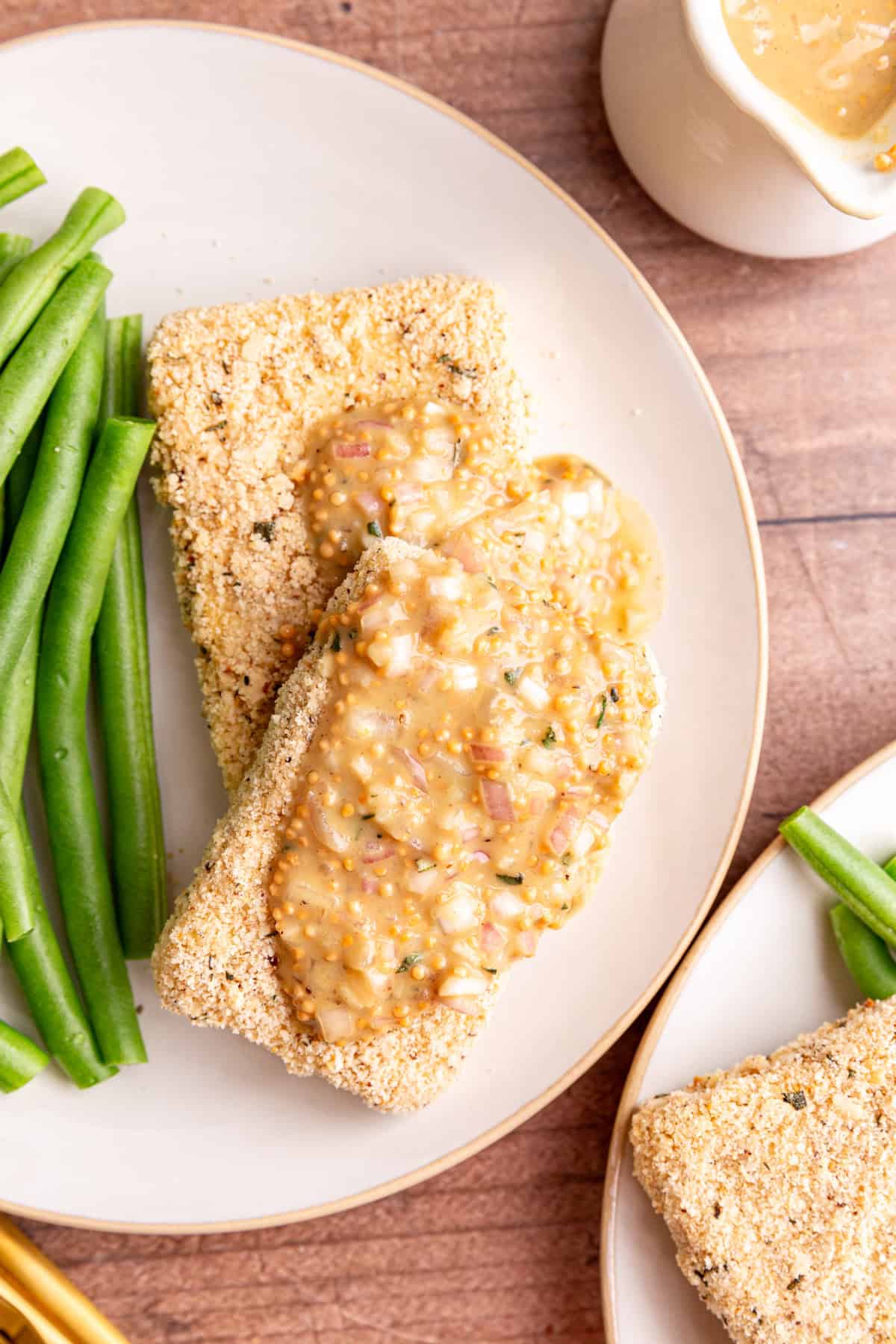 Two tofu cutlets on a plate, with a generous drizzle of mustard vinaigrette, and green beans on the side.