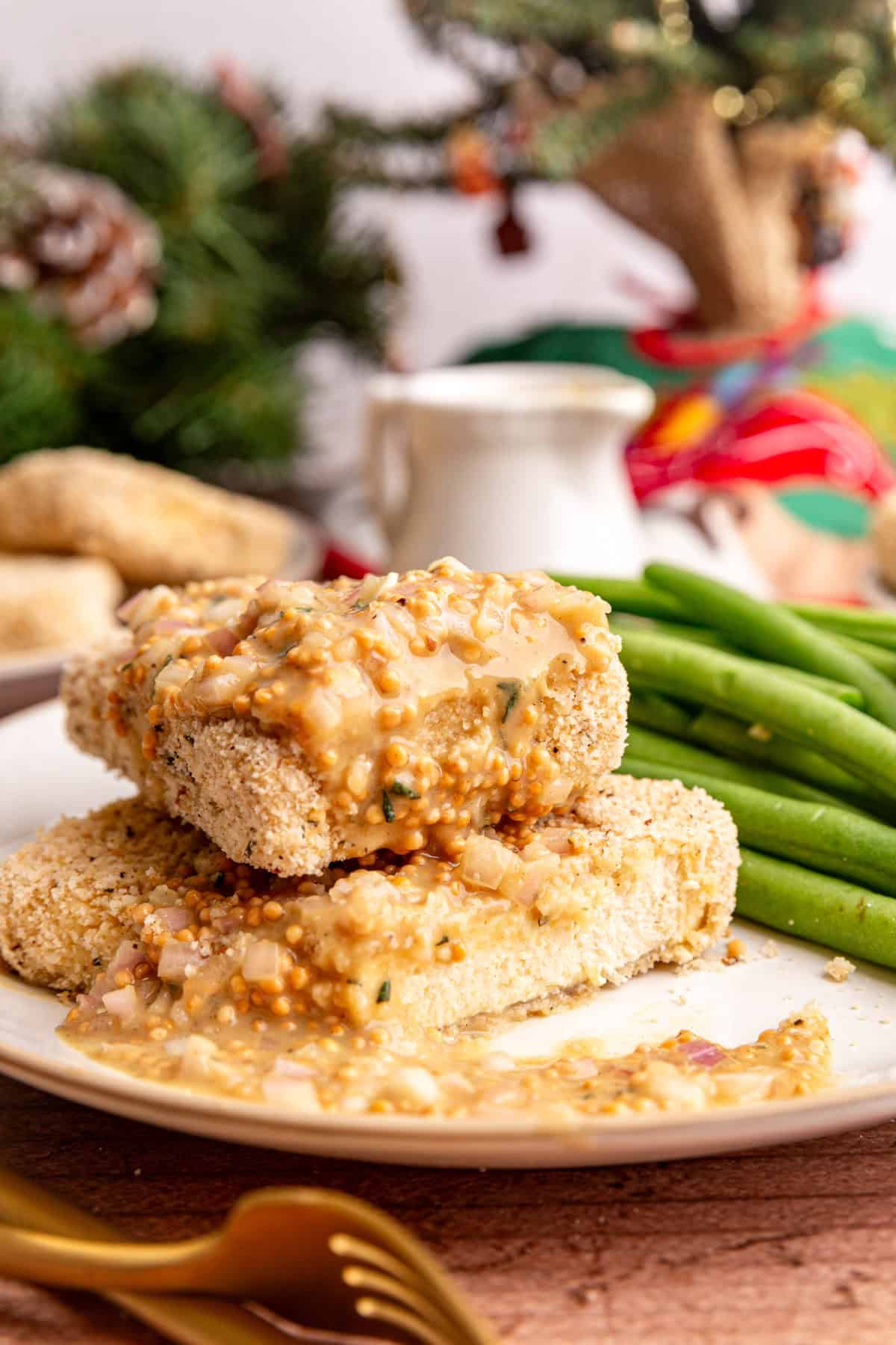 Two tofu cutlets on a plate, with a generous drizzle of mustard vinaigrette, on cutlet has been sliced into.