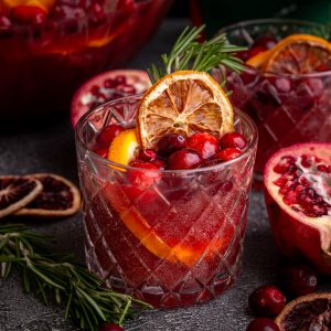 A glass of Non-Alcoholic Christmas Punch, garnished with rosemary and dried orange.
