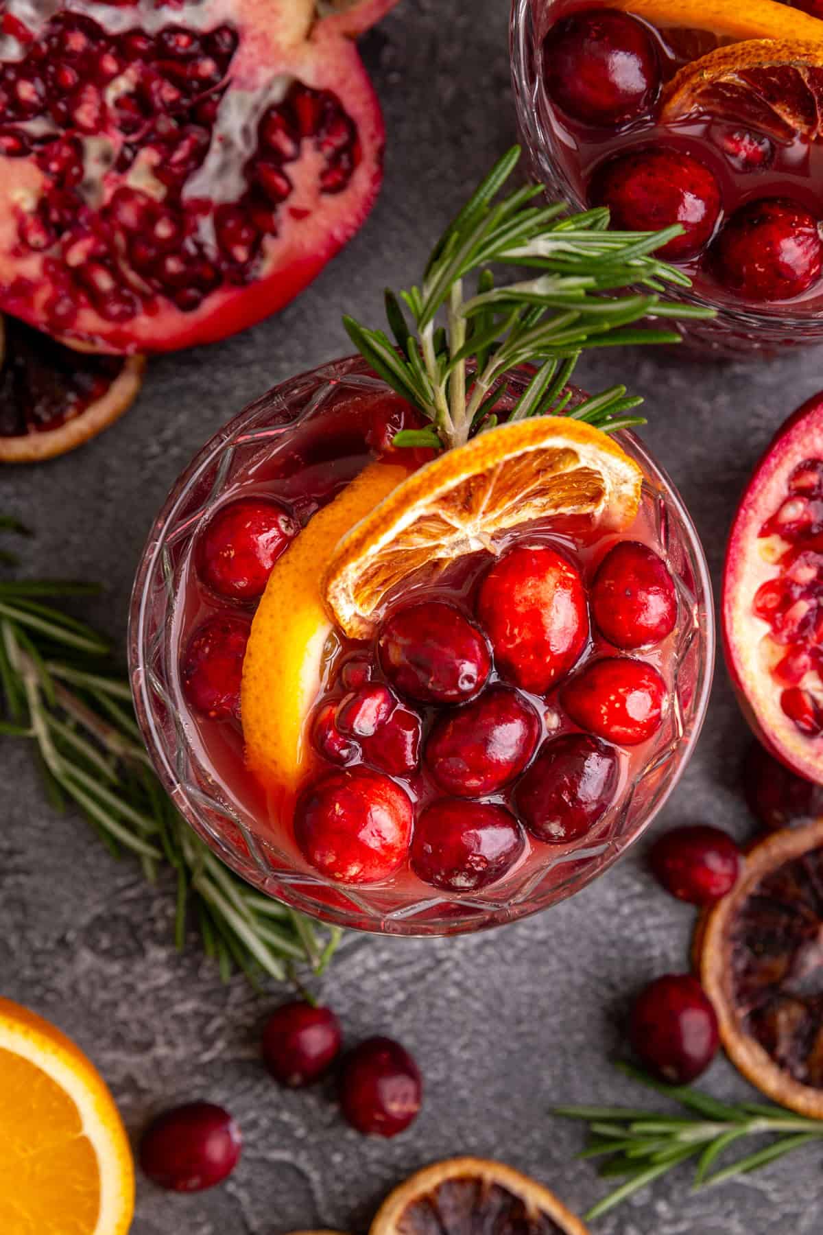 A top-down view of a glass of Christmas punch, with oranges, rosemary, and cranberries in the glass.