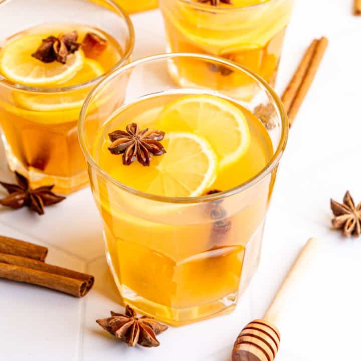 Several glasses hot toddies, garnished with lemon slices and star anise.