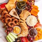A vegan charcuterie board on a countertop with plates and drinking glasses.