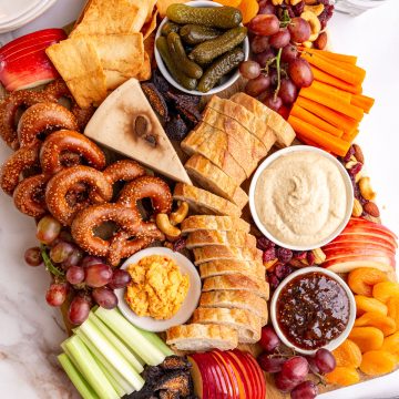 A vegan charcuterie board on a countertop with plates and drinking glasses.