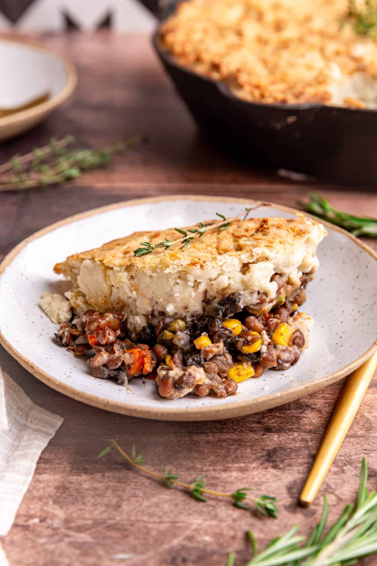 A slice of vegan lentil shepherd's pie, with the pan of pie behind the bowl.