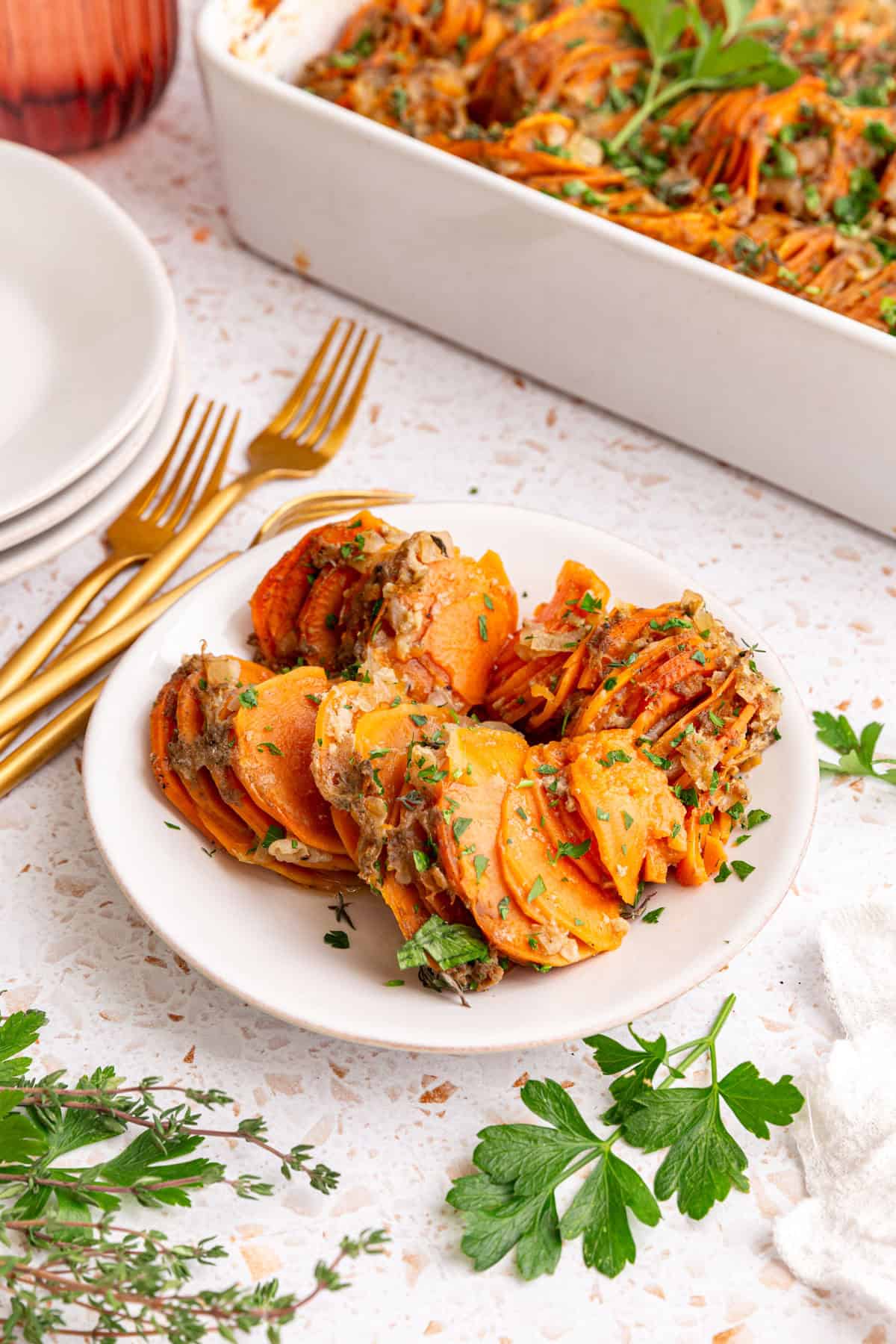 A plate of vegan sweet potato gratin, next to a casserole dish of gratin.