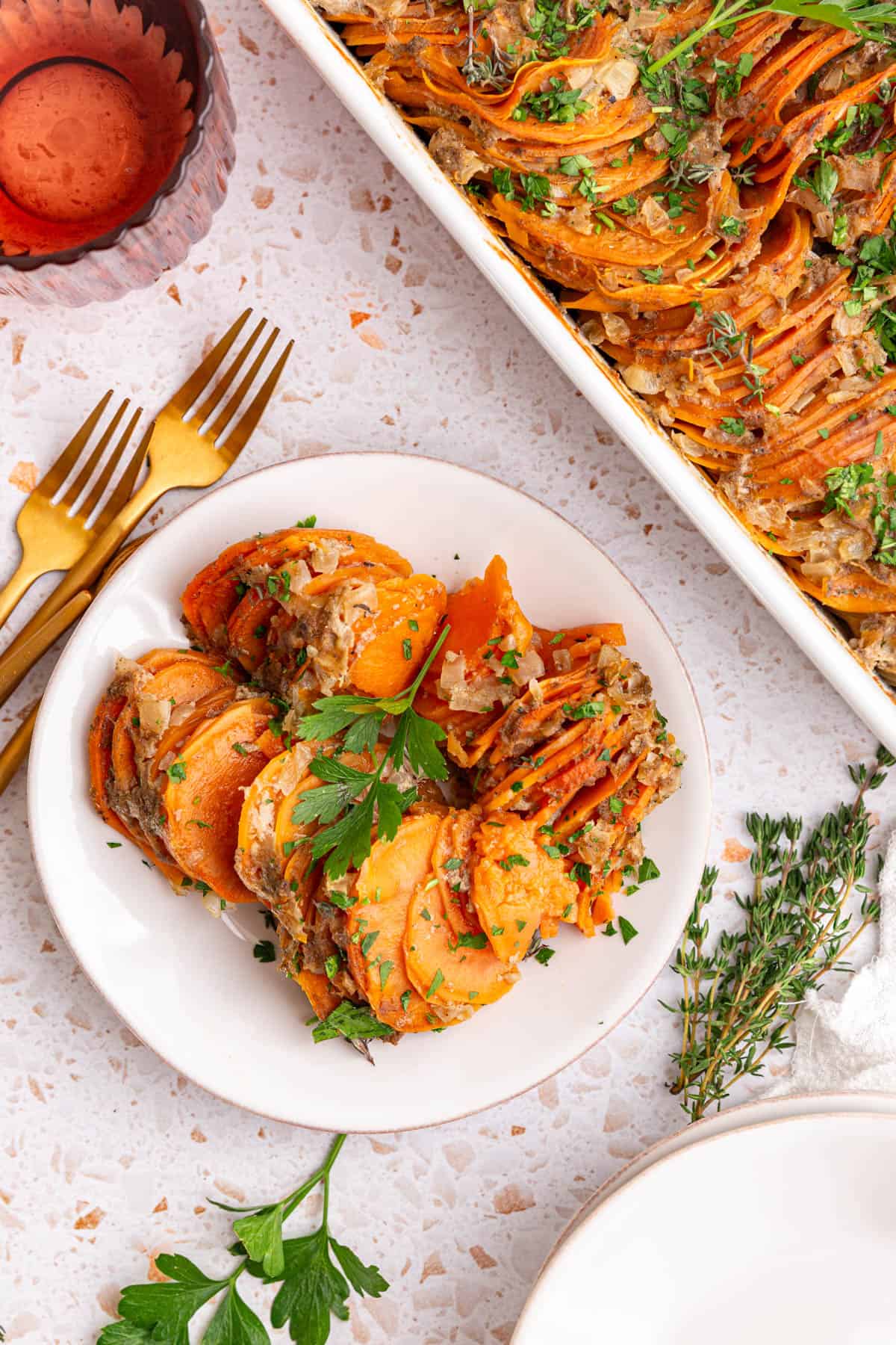 A plate of vegan sweet potato gratin, next to a casserole dish of gratin.