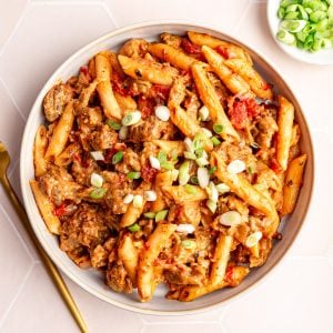 A bowl of vegan Cajun chicken pasta, with a bowl of scallions.