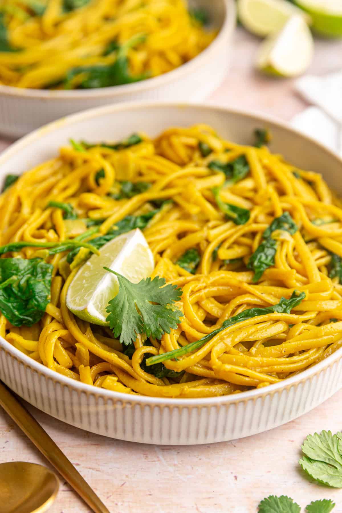 A bowl of vegan curry pasta, garnished with a lime wedge and cilantro.