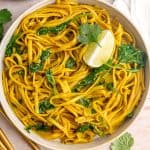 A bowl of vegan curry pasta, garnished with a lime wedge and cilantro.
