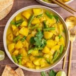 A bowl of green bean potato curry, with pita, cilantro, and lime wedges.