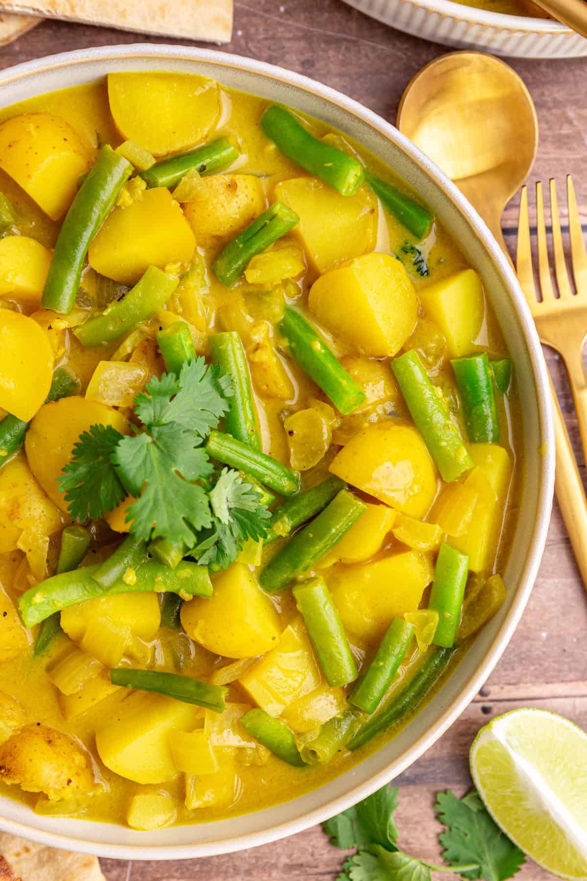 A bowl of green bean potato curry, with a knife and fork, ready to eat.