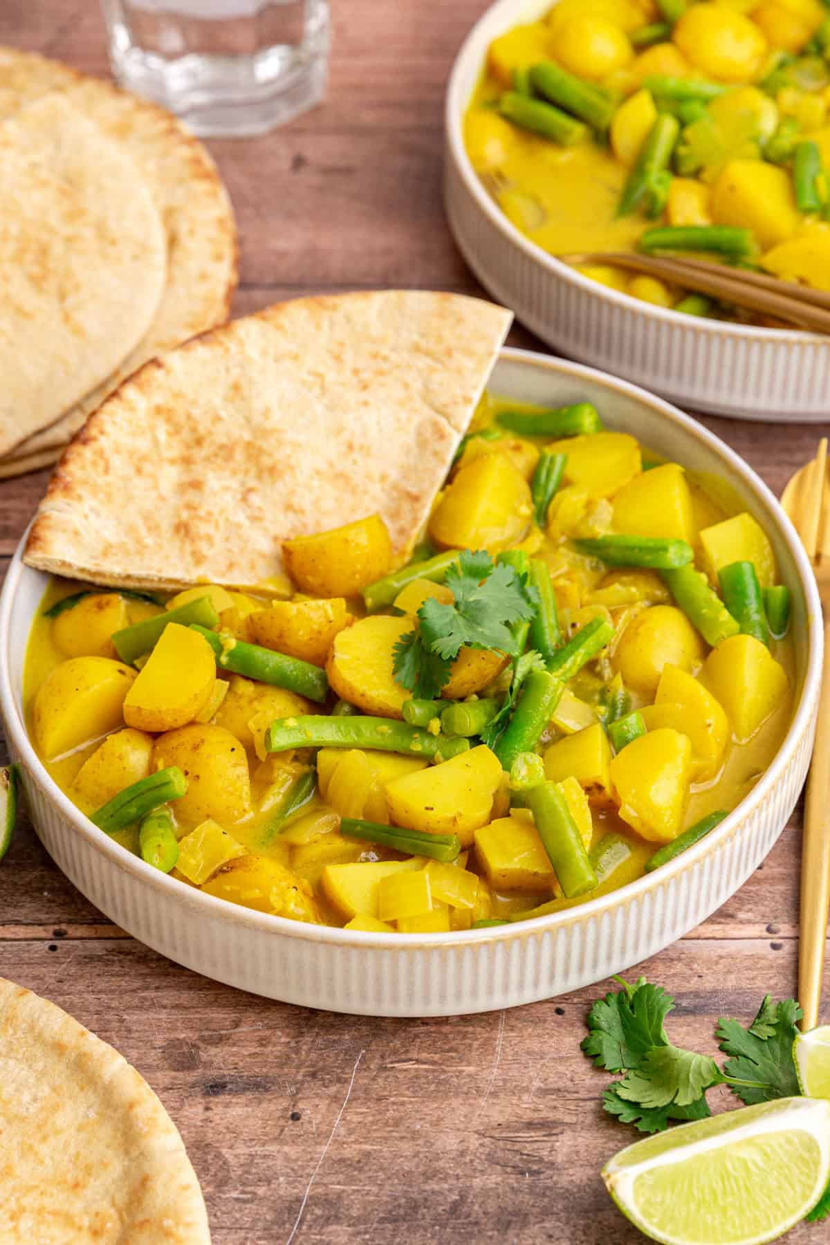 A bowl of green bean potato curry with a slice of pita in the bowl.