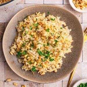 A plate of vegan rice pilaf, garnished with pine nuts and fresh parsley.