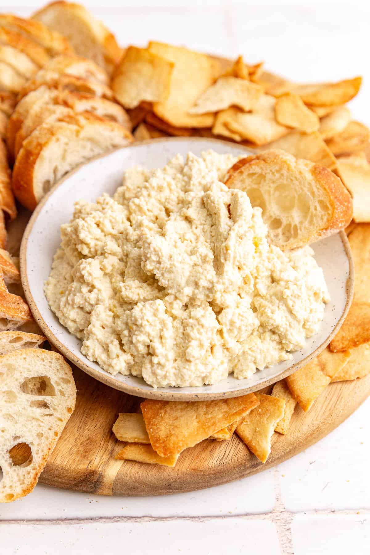 A bowl of tofu ricotta with a piece of baguette dipped in.