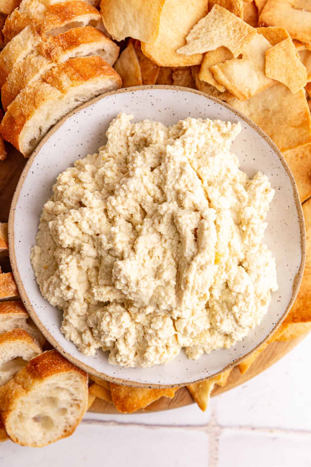 A bowl of tofu ricotta on a platter of pita chips and bread.