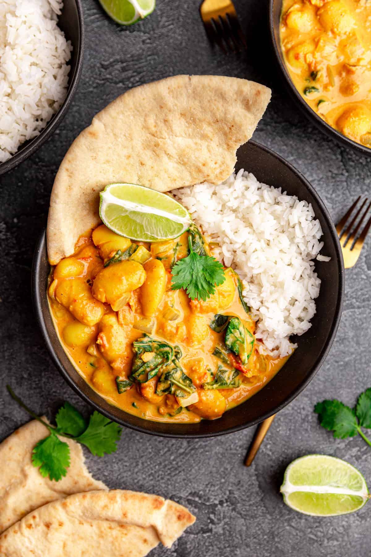 A bowl of rice, butter bean curry, and pita, with a lime wedge.