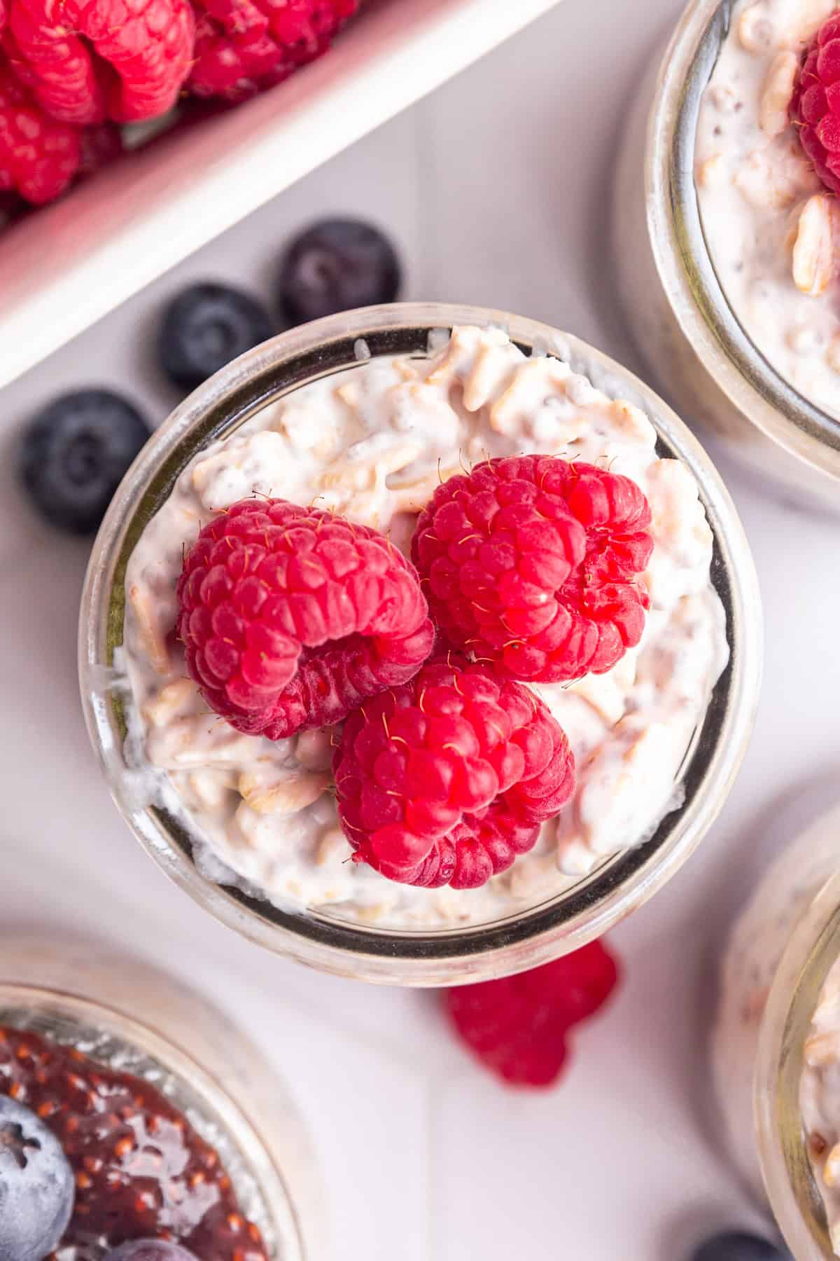 A top-down view of a jar of coconut milk overnight oats, topped with raspberries.