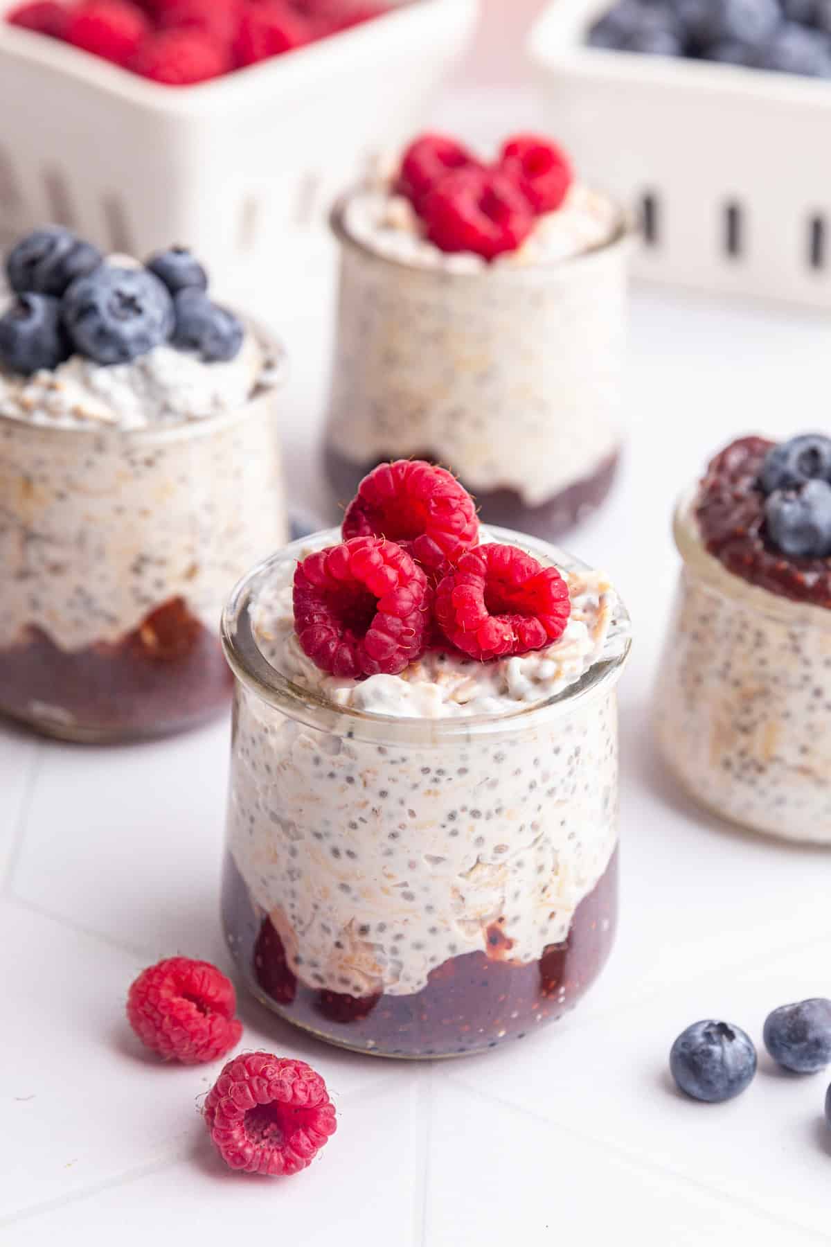 A jar of coconut milk overnight oats with jam on the bottom and raspberries on top.