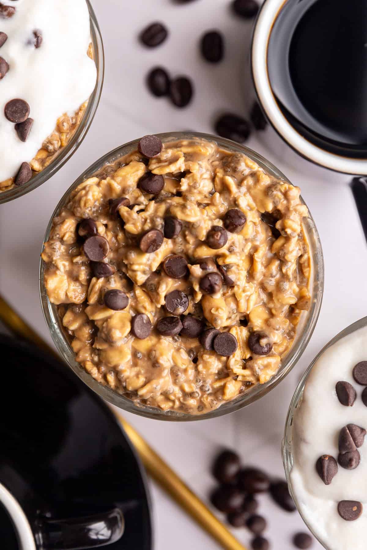 A top-down view of several jars of coffee overnight oats, topped with yogurt and chocolate chips.