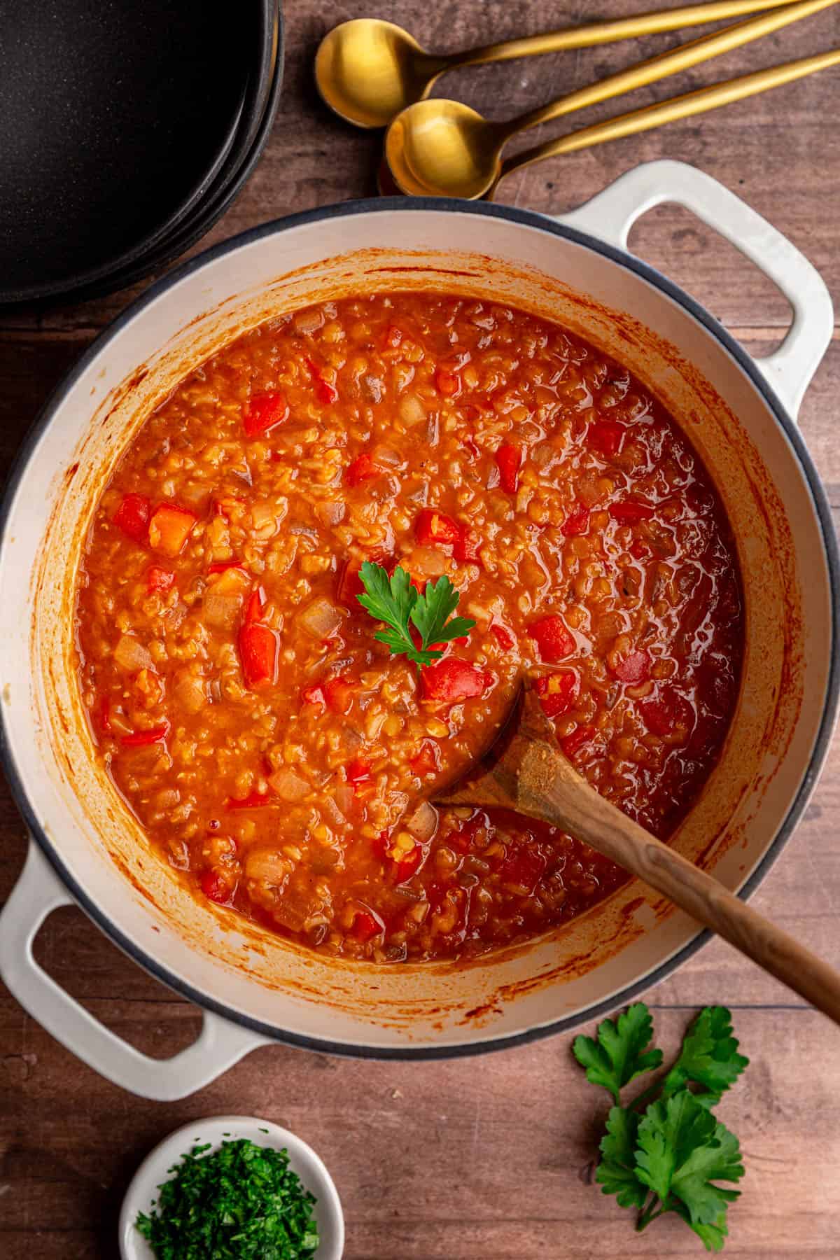 A pot of freshly cooked Red Pepper Red Lentil Soup, with a wooden spoon, ready to serve.