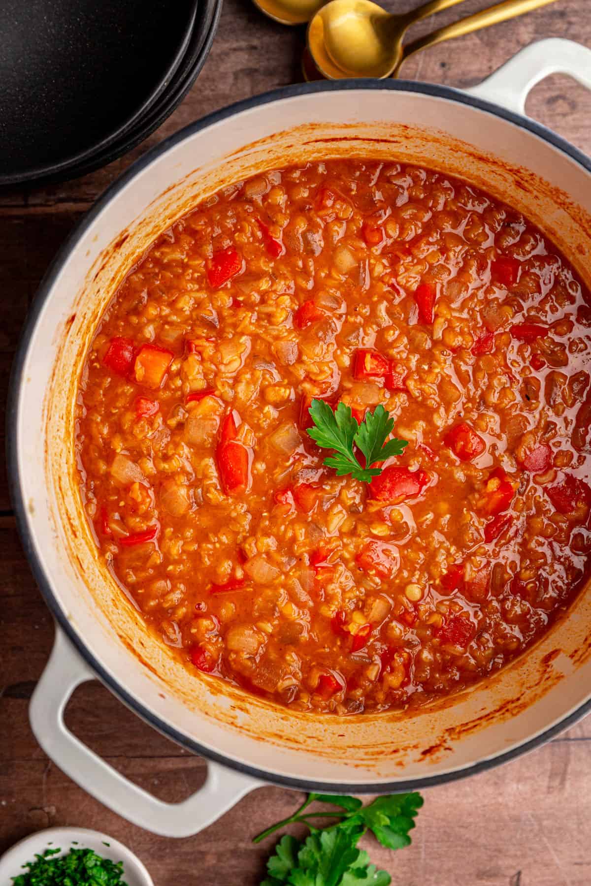A pot of Red Pepper Red Lentil Soup, garnished with a parsley leaf.