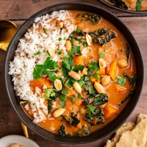 A bowl of Vegan African Peanut Stew, served over rice, garnished with cilantro and peanuts.