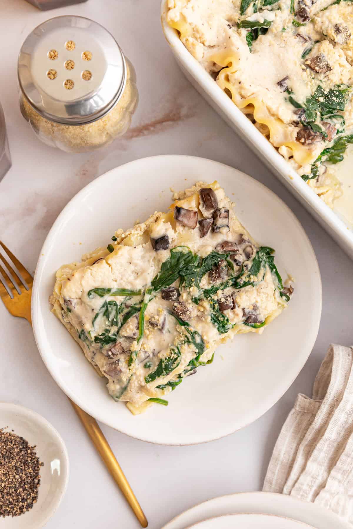 A plate with a serving of white lasagna, topped with vegan parmesan.