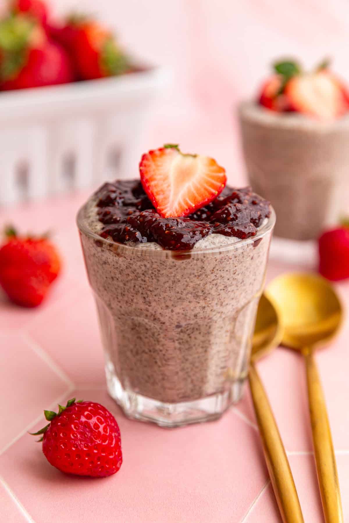A jar of blended chia pudding, topped with jam and a strawberry.