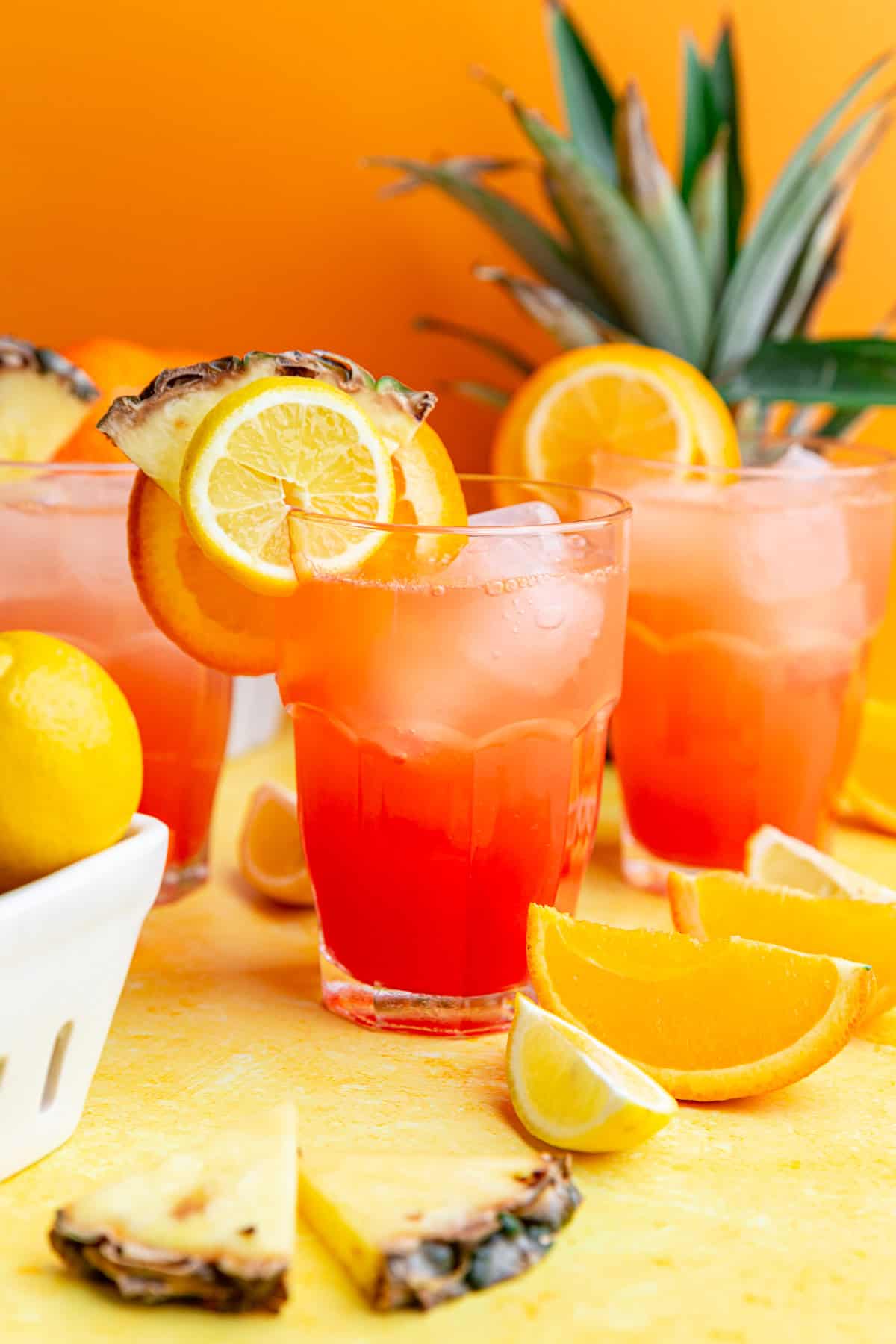 Several glasses of cinderella mocktail garnished with lemon, orange, and pineapple slices.