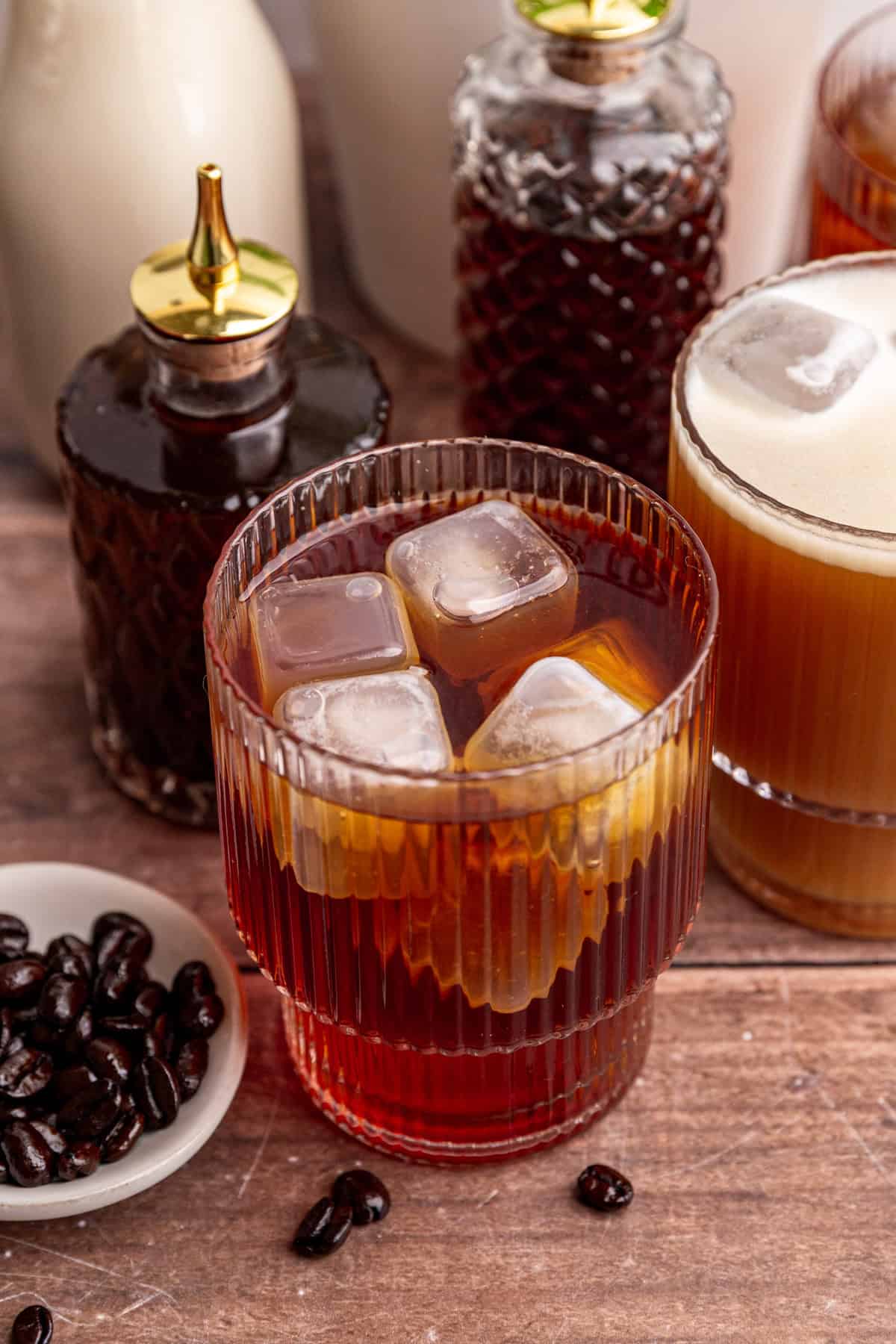 A glass of decaf cold brew on a table with coffee syrups.
