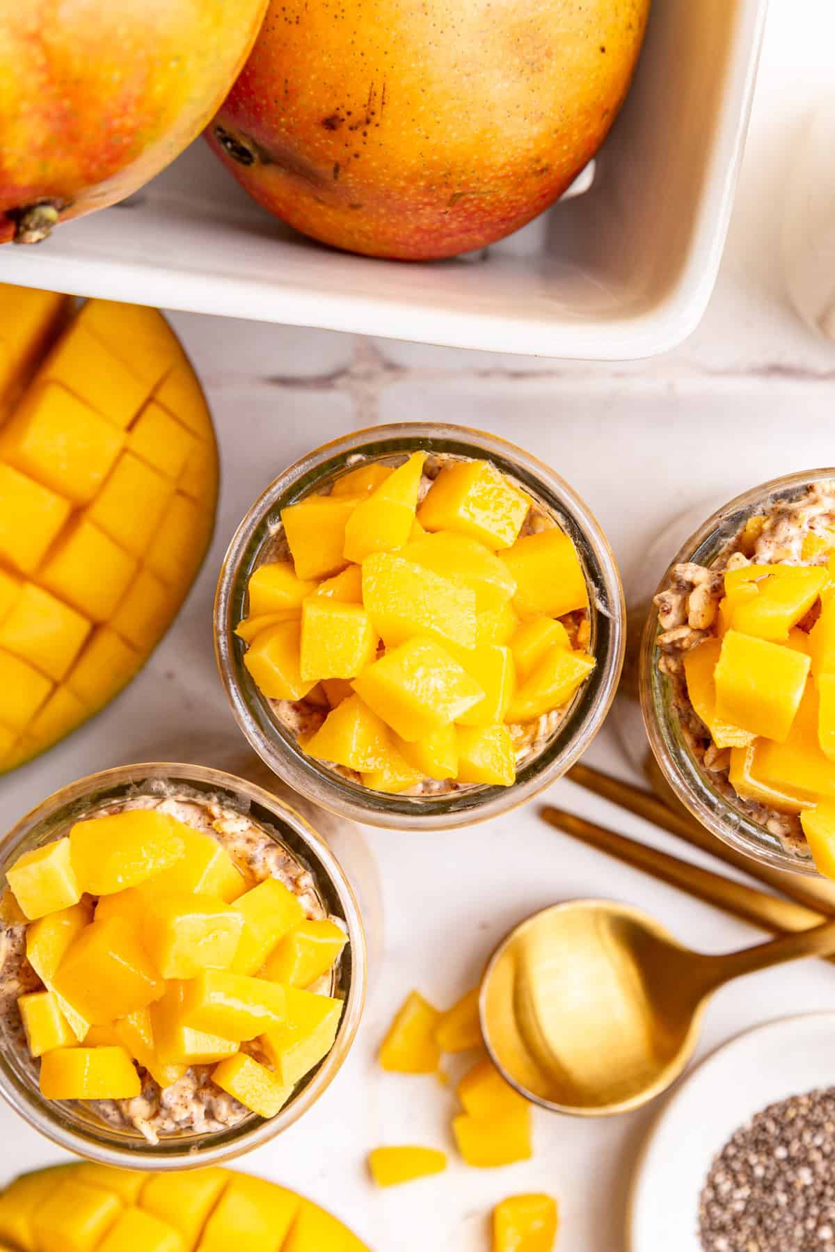 Several jars of mango overnight oats, with a berry box of ripe mangos.
