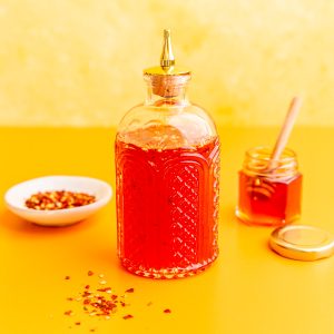 A jar of vegan hot honey, with a jar of honey and red pepper flakes.