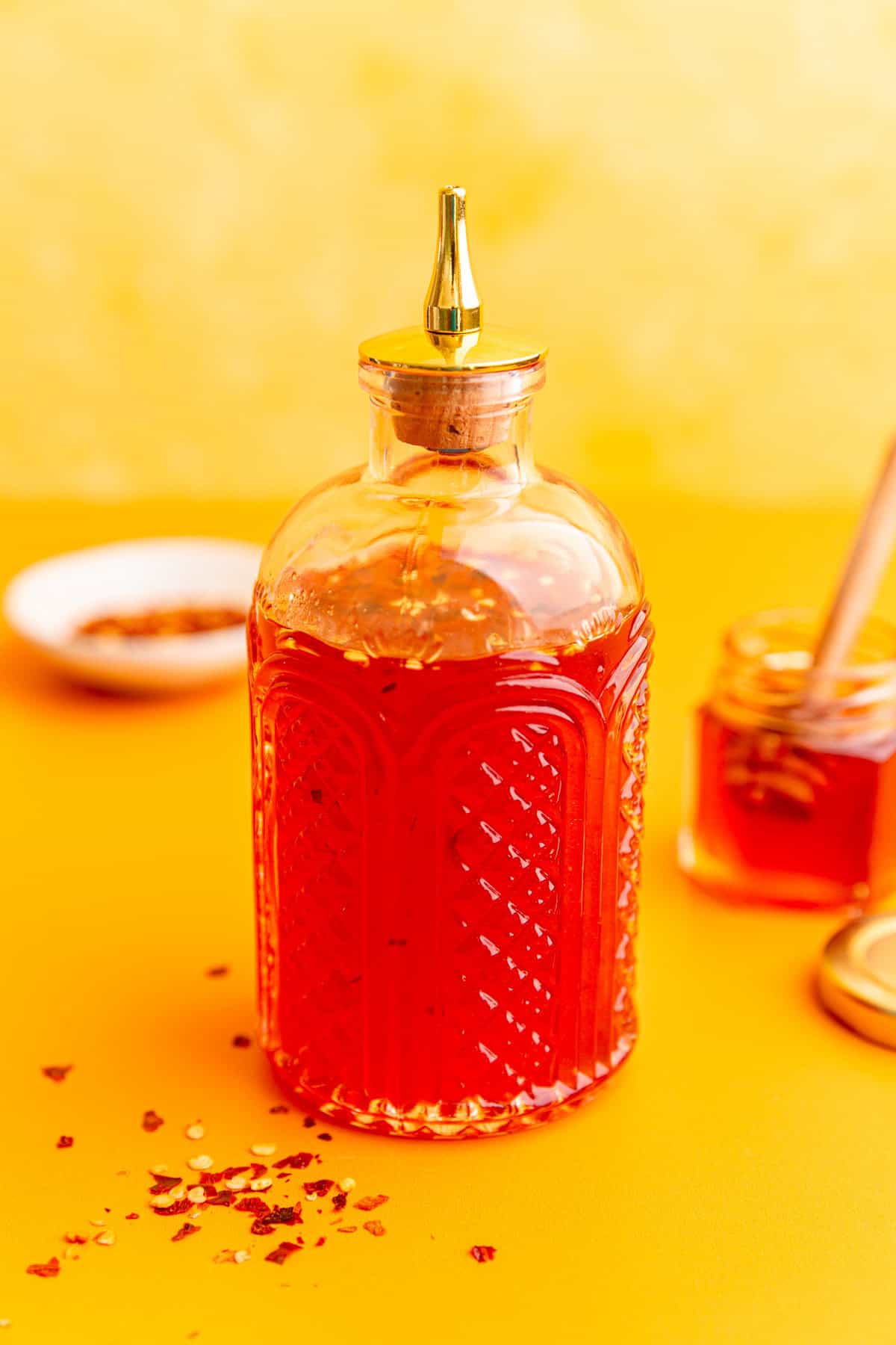 A jar of vegan hot honey, with a jar of honey and red pepper flakes.