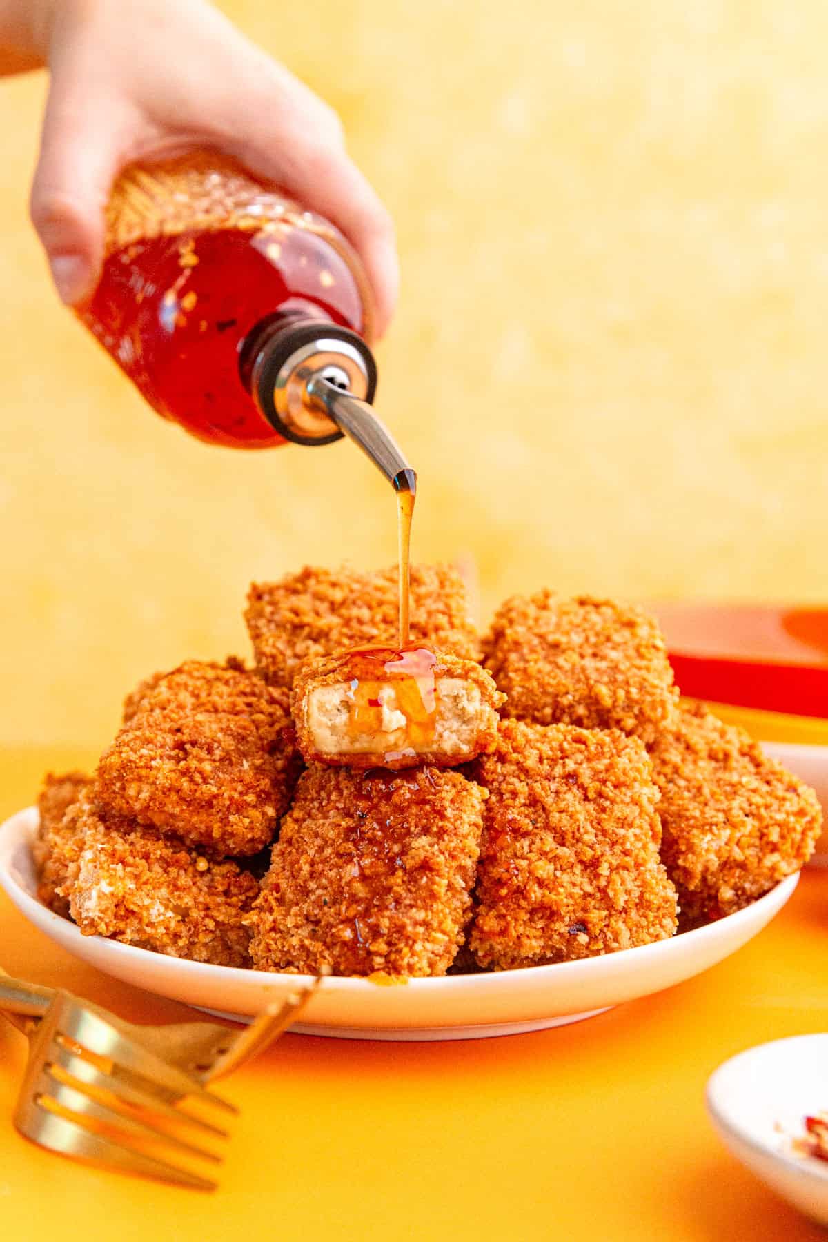 Vegan hot honey being drizzled onto a plate of hot honey tofu.