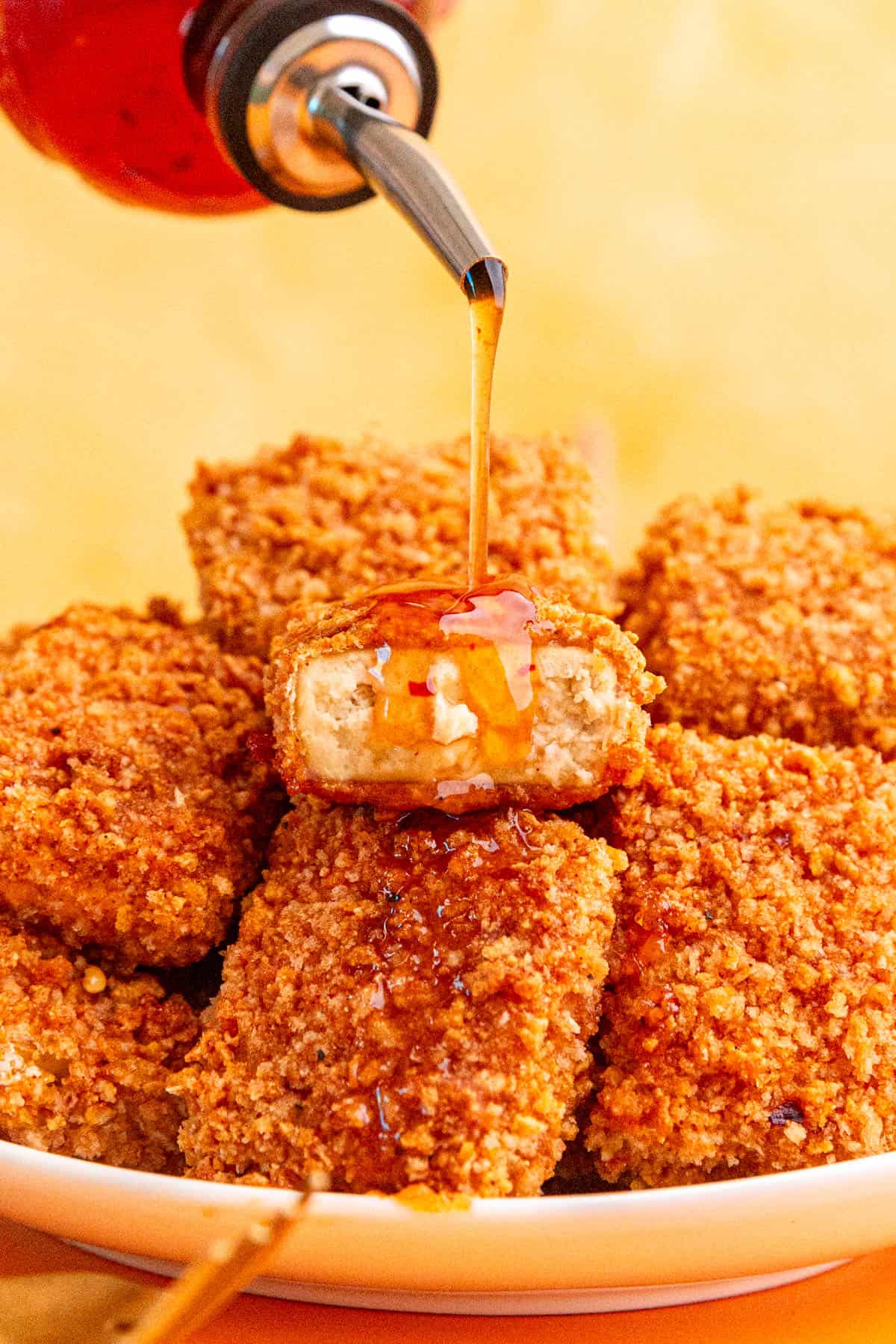 Vegan hot honey being drizzled onto a plate of hot honey tofu.