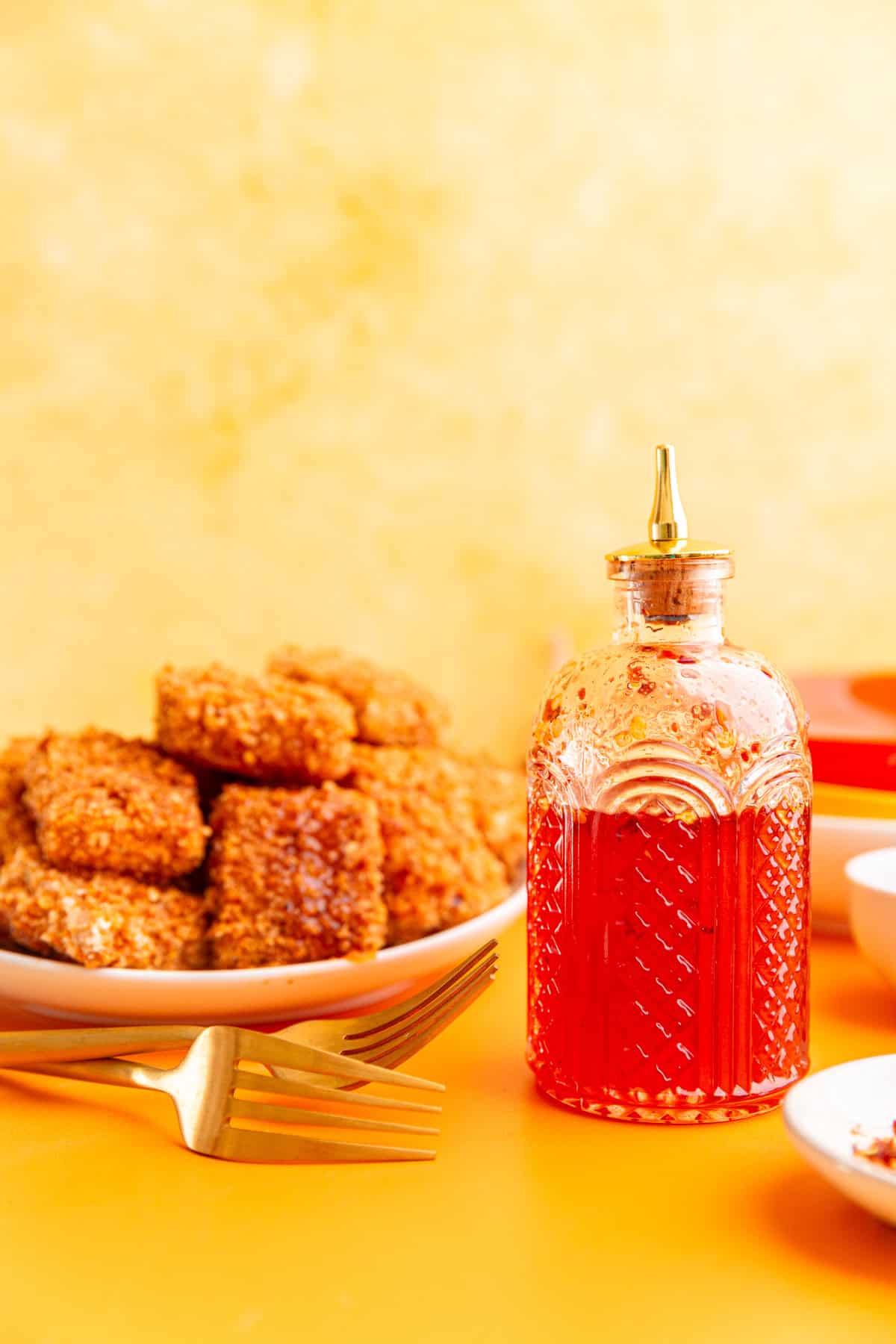 A jar of vegan hot honey with a plate of hot honey tofu.