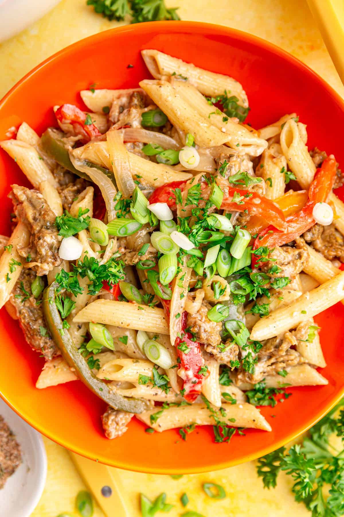 A bowl of vegan rasta pasta, topped with parsley and scallions, ready to eat.