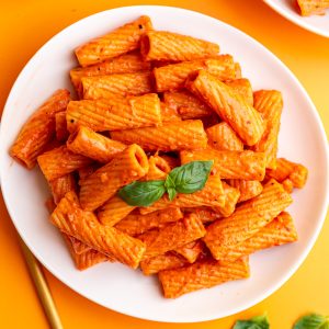 A plate of vegan vodka pasta, with a garnish of fresh basil, ready to eat.