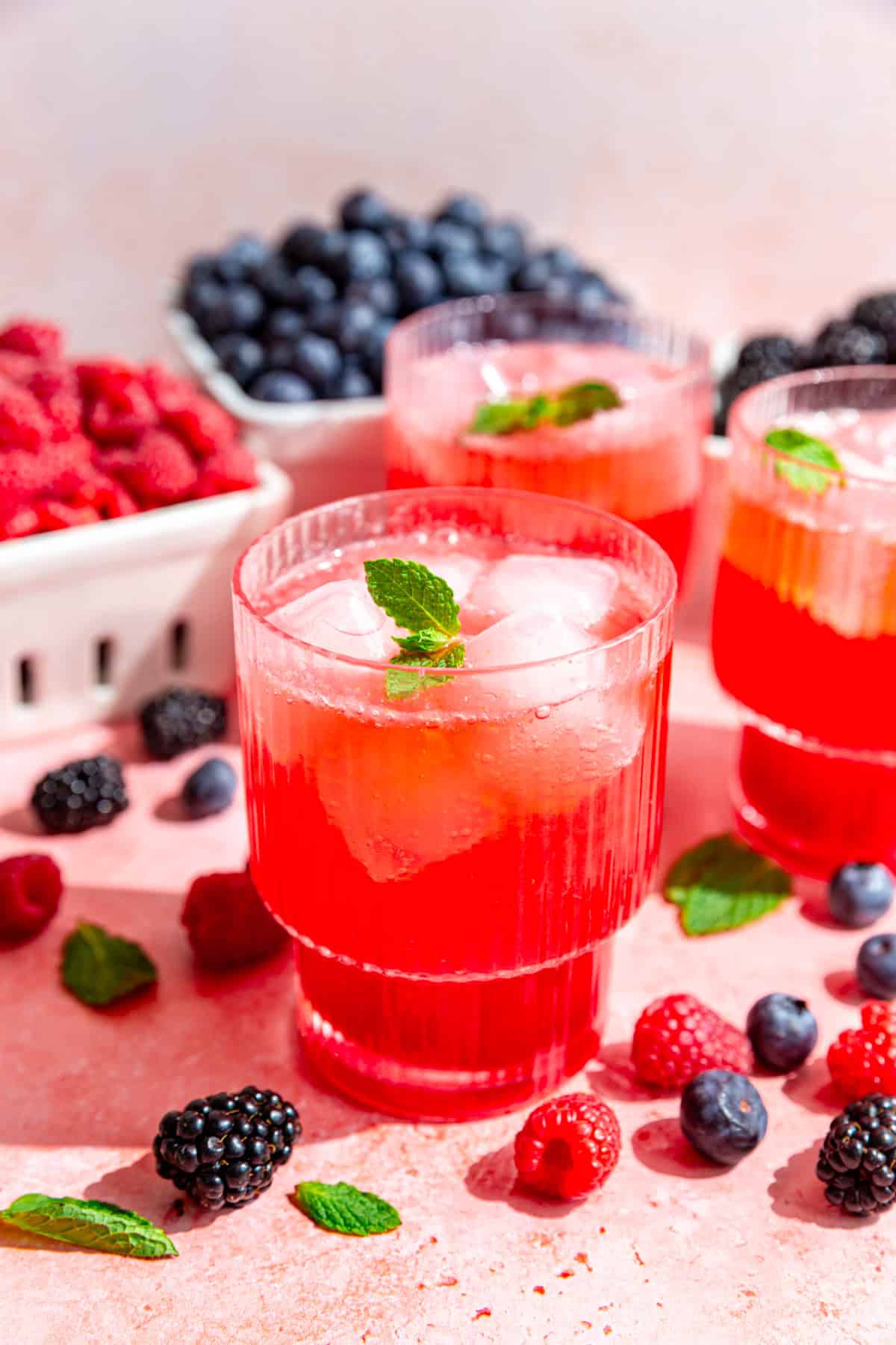 A glass of mixed berry mocktail, garnished with fresh mint and surrounded by boxes of fresh berries.