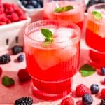 A glass of mixed berry mocktail, garnished with fresh mint and surrounded by boxes of fresh berries.