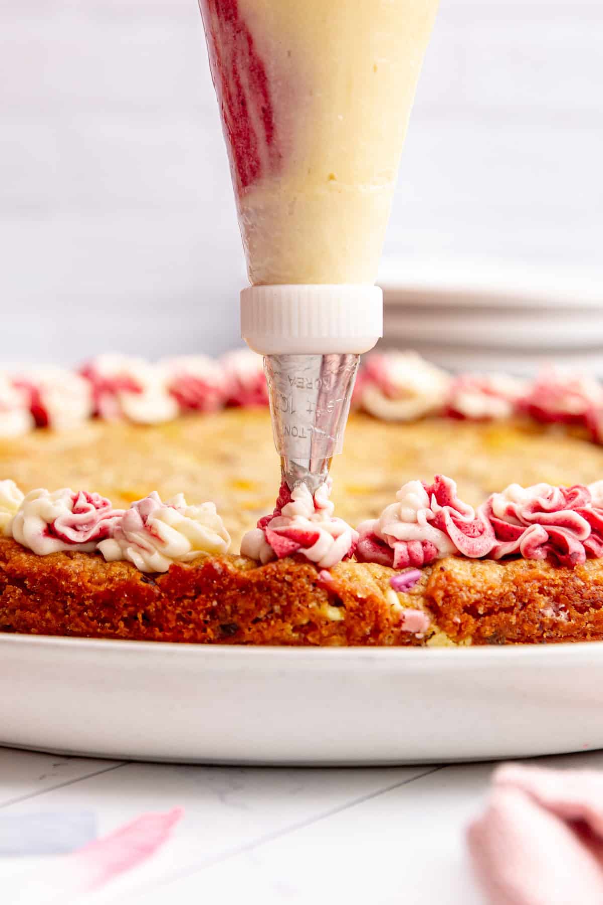 A piping bag of vegan buttercream, frosting a cookie cake.