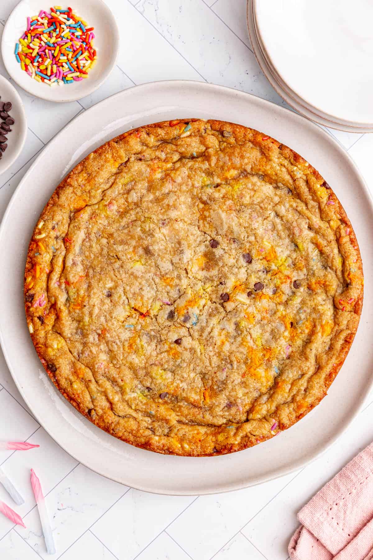 An unfrosted vegan cookie cake on a plate with sprinkles and birthday candles next to the plate.