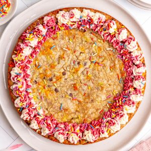 A vegan cookie cake decorated with pink and white frosting around the borders and sprinkles.