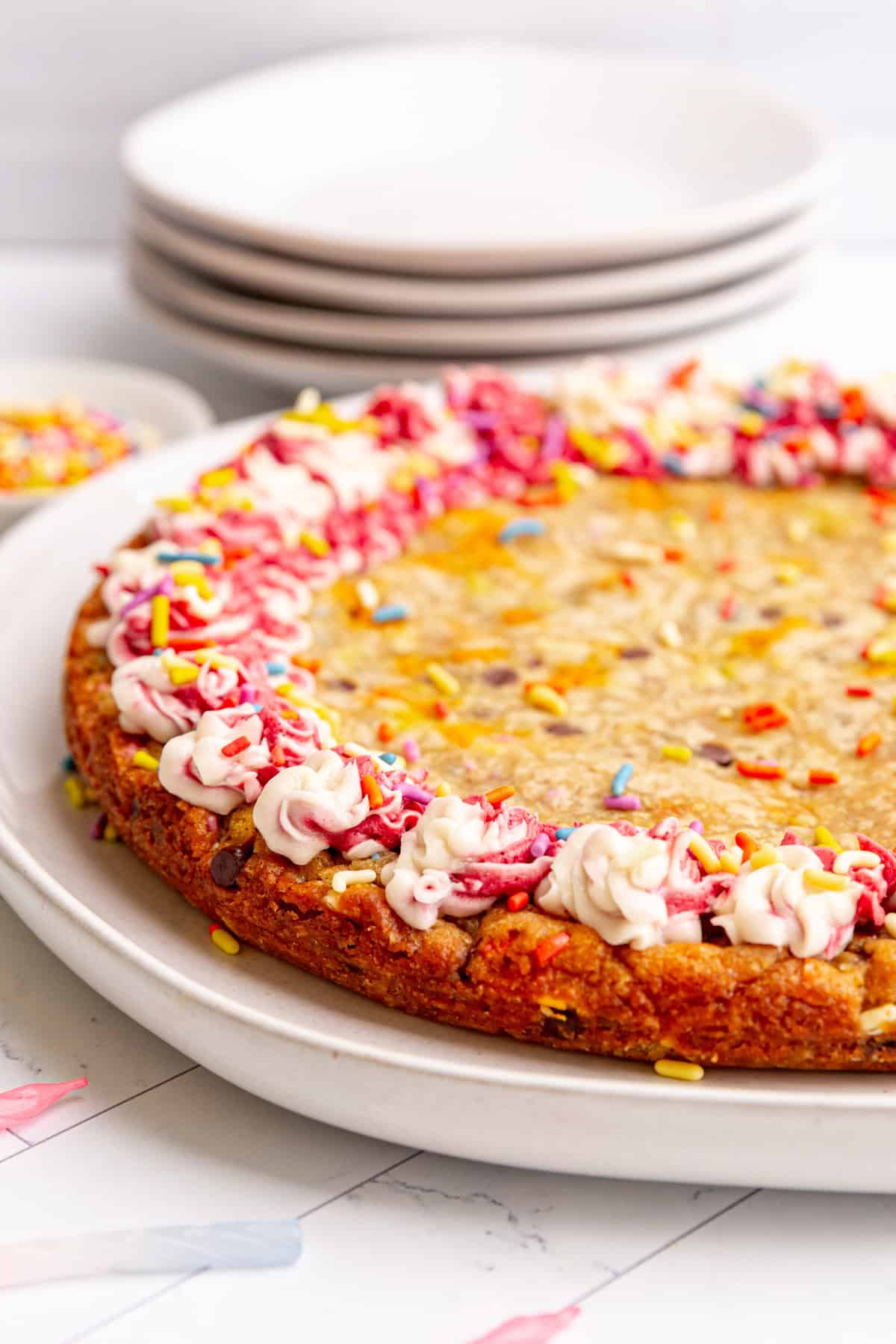 A vegan cookie cake decorated with pink and white frosting around the borders and sprinkles.