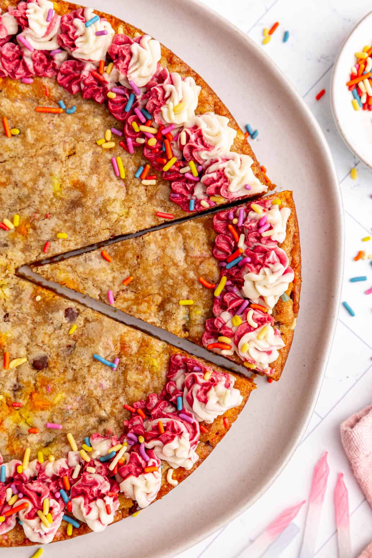 A slice cut out of a vegan cookie cake, with candles and sprinkles next to it.